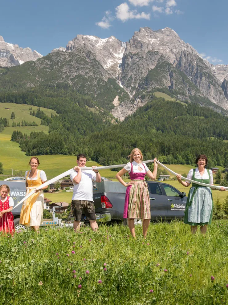 Group in traditional Austrian clothing holding a long hose with Alpine mountains in background